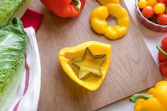 a cutting board topped with bell peppers and star shaped cookie cutters next to other vegetables