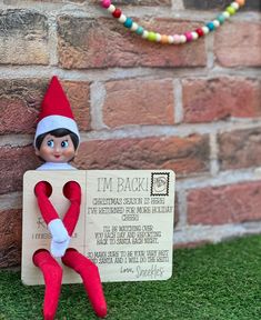 an elf sitting on top of a sign next to a brick wall with the words i'm back