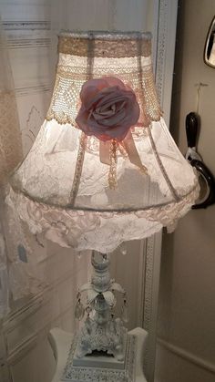 a lamp that is on top of a table with a rose on the shade and lace around it