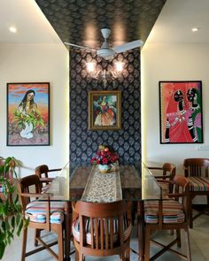 a dining room table with chairs and paintings on the wall behind it, along with potted plants