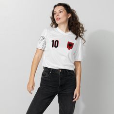 a woman standing in front of a white wall wearing jeans and a t - shirt with the number 10 on it