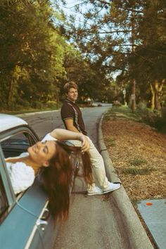 two people sitting on the hood of a car