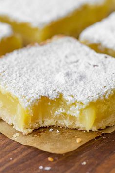 two pieces of lemon bars sitting on top of a wooden cutting board with powdered sugar