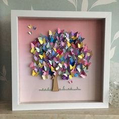 a paper tree with butterflies on it in a white box frame next to a vase