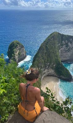 a woman sitting on top of a cliff overlooking the ocean