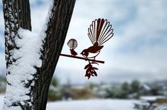 a metal bird sitting on top of a tree branch next to snow covered ground with trees in the background