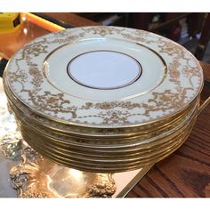 a stack of gold and white plates sitting on top of a wooden table next to a vase