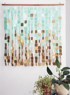 a wall hanging made out of gold and green tiles next to a potted plant