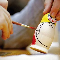 a child is holding a paintbrush and painting a paper doll with a red nose