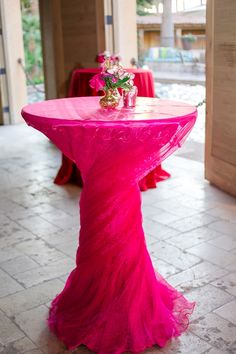 a pink table with flowers on it in the middle of a room filled with red chairs