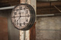 an old clock hanging from the side of a pole in a room with exposed pipes