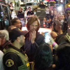 a group of people standing around each other in front of a police officer talking on a cell phone