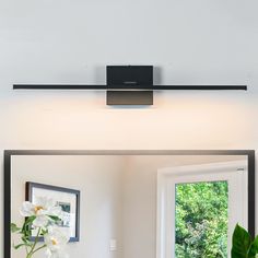 a bathroom light that is on above a mirror with flowers in the vase next to it