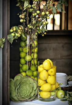 a vase filled with lots of yellow lemons next to a pile of green apples