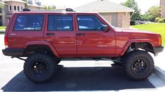 a red jeep is parked on the side of the road in front of a house