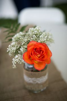 an orange rose in a glass vase with baby's breath on the table top