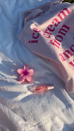 a pink flower laying on top of a white towel next to a bottle of lip gloss