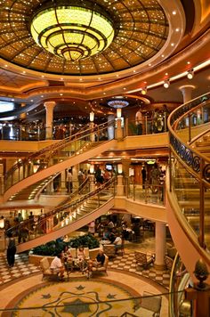 the inside of a cruise ship with people sitting at tables and stairs on each side