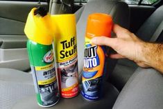 a hand holding an orange bottle and two bottles of cleaner on the back seat of a car