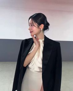 a woman standing in front of a white wall wearing a black blazer and dress