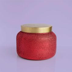 a red candle with a gold lid on a purple background, it looks like something out of space