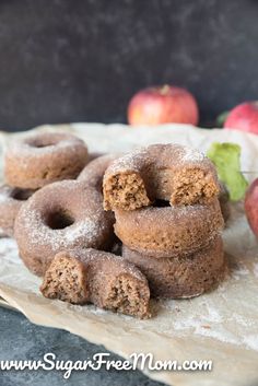 some sugared doughnuts are on a piece of parchment paper with apples in the background