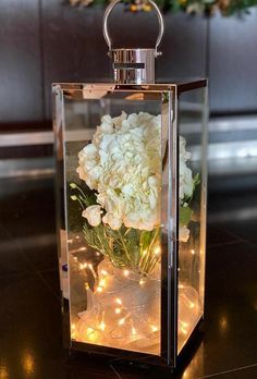 a vase filled with white flowers sitting on top of a wooden table next to lights