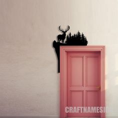 a pink door with a deer on the top and pine trees behind it, in front of a white wall