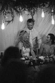 a bride and groom cutting their wedding cake at the reception table with guests sitting around