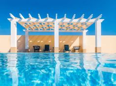 an empty swimming pool with lounge chairs and a pergolated roof over the water