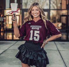 a woman in a football uniform holding up a cup and posing for the camera with her hands on her hips