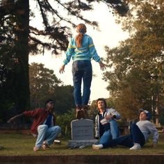 a group of people sitting on the ground in front of a grave with one person standing up