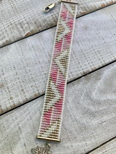 a pink and white beaded bracelet sitting on top of a wooden table next to a keychain