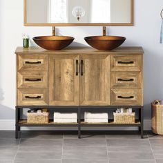 a bathroom vanity with two bowls on top and a mirror above it, in front of a white wall