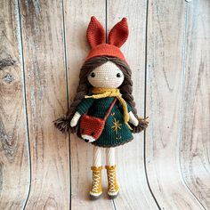 a crocheted doll with brown hair wearing a green dress and yellow boots on a wooden surface