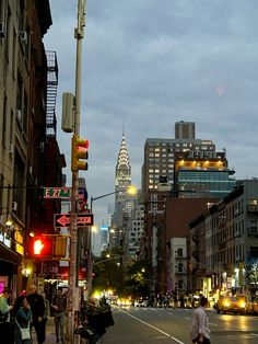 people are walking down the street in front of tall buildings and skyscrapers at night