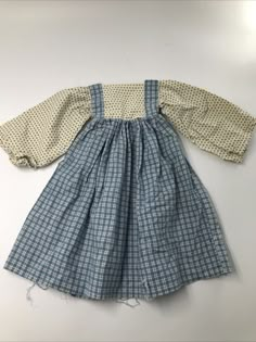 an old fashioned blue and white checkered dress with long sleeves, is laying on the floor