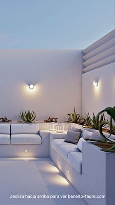 a living room filled with lots of white furniture next to potted plants and lights