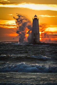 a light house in the middle of an ocean with waves crashing against it and sun setting