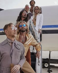 a group of men standing on the steps of an airplane with one man wearing sunglasses