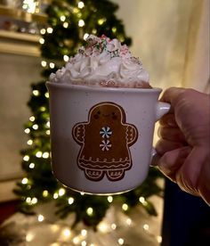 a hand holding up a cup with whipped cream and a gingerbread cookie on it