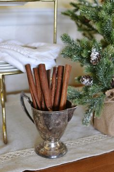 a silver cup filled with cinnamon sticks on top of a table next to a christmas tree