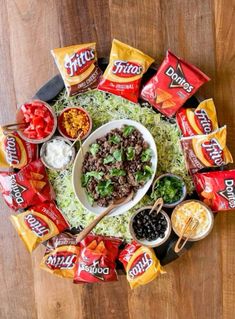 a platter filled with chips, salad and dips on top of a wooden table