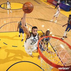 a basketball player dunking the ball in front of other players on a hardwood court