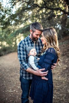 a man and woman holding a baby in their arms while standing on a dirt road