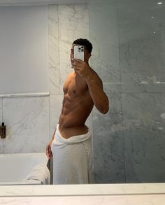 a shirtless man taking a selfie in front of a bathroom mirror with his cell phone