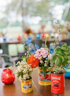 three tin cans with flowers in them sitting on a table