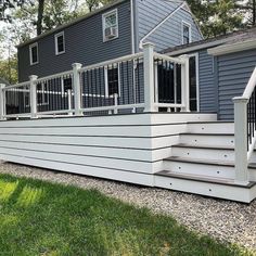 a white deck with railings and steps in front of a blue house on a sunny day