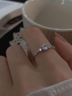 a woman's hand with a diamond ring on her finger next to a coffee cup