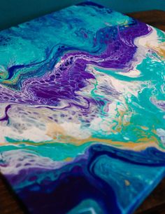 an abstract painting on a wooden table with blue, yellow and purple paint swirled over it